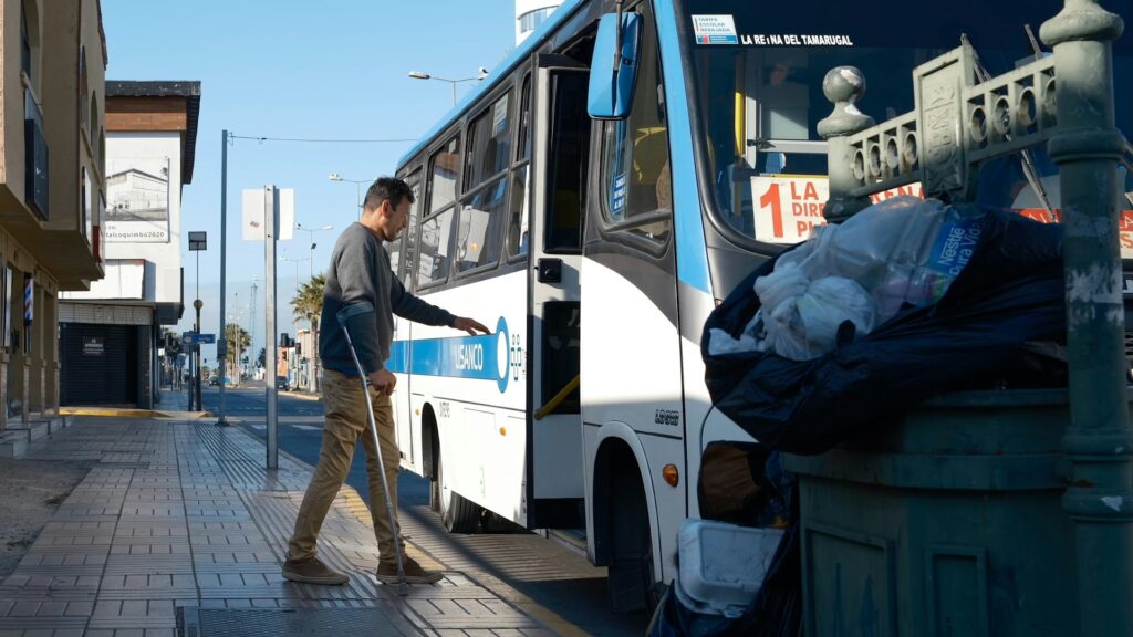 Man with cane boarding a bus on a sunny day.